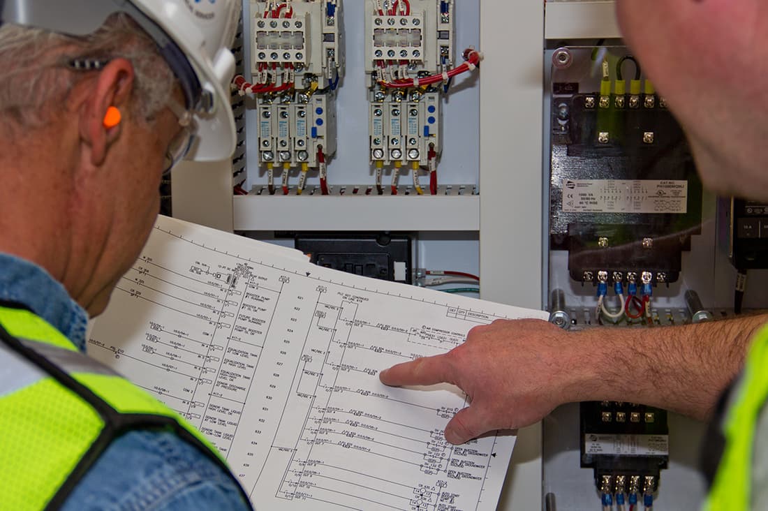 A finger tracing a rung on a ladder wiring schematic posted inside a control panel.