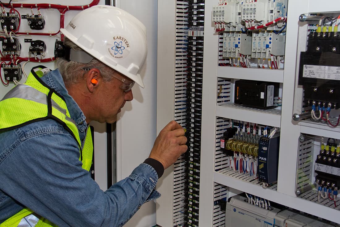 A Karsten electrician in a company hard hat working at a terminal rail inside a control panel.
